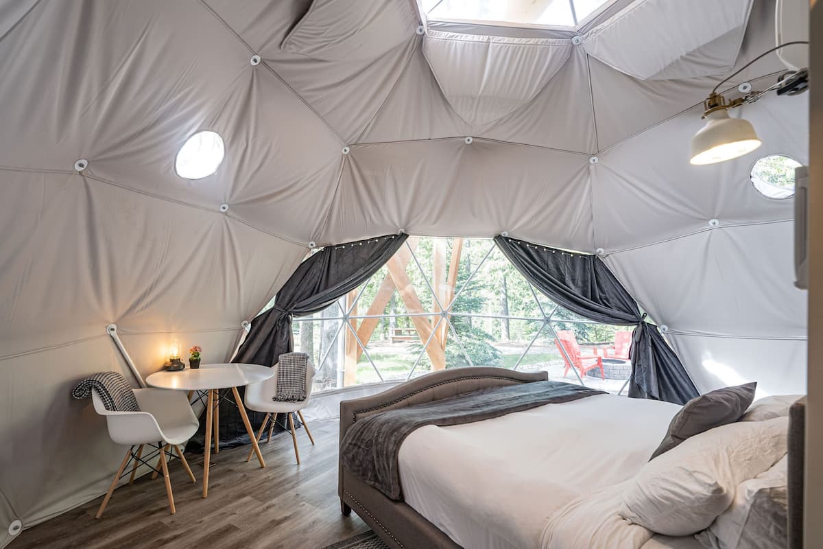 A tent-style room with a bed, a table with chairs, and a window with curtains.