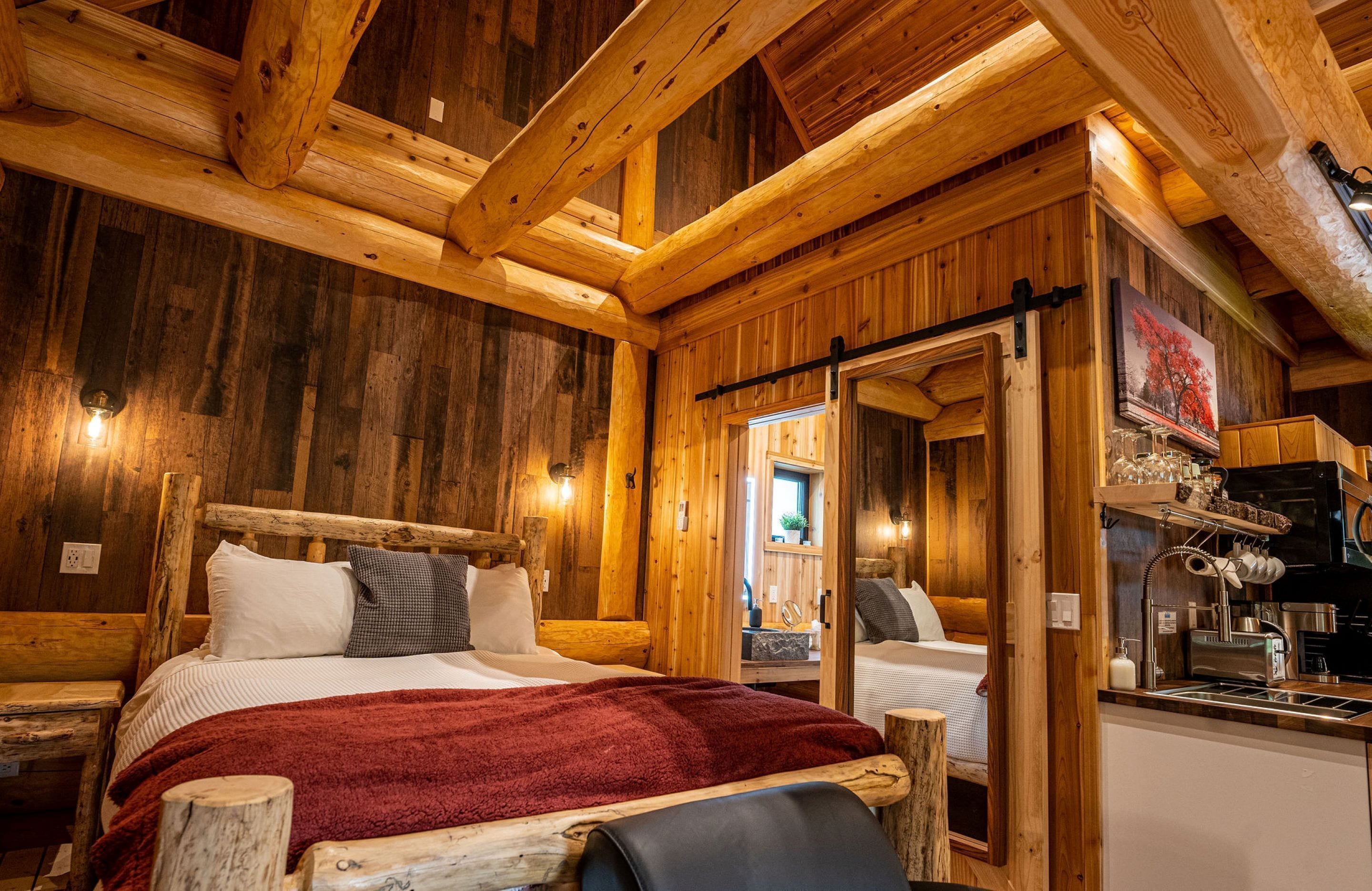 A wooden cabin interior with a bed, a small kitchenette, and a wooden ceiling.