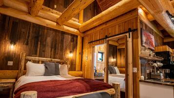 A wooden cabin interior with a bed, a small kitchenette, and a wooden ceiling.
