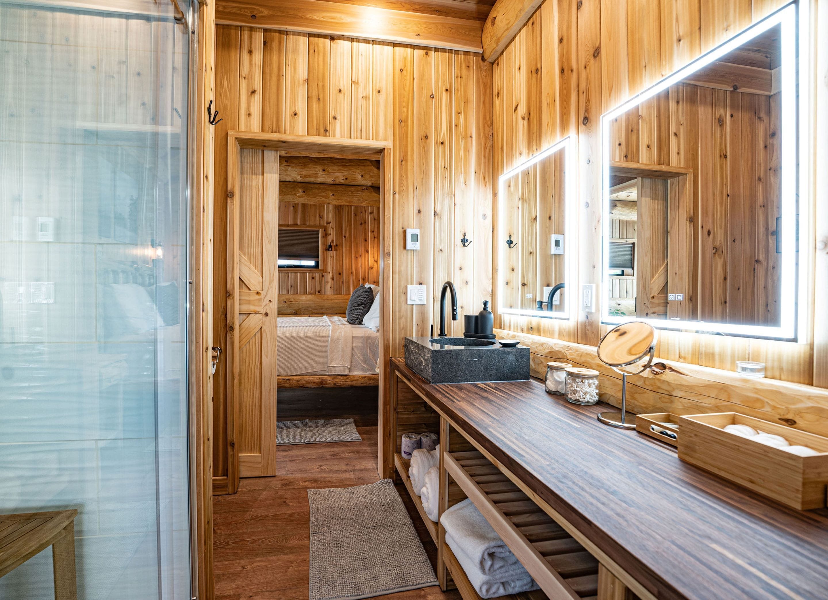 A wooden cabin interior with a bed, a sink, and a large mirror.