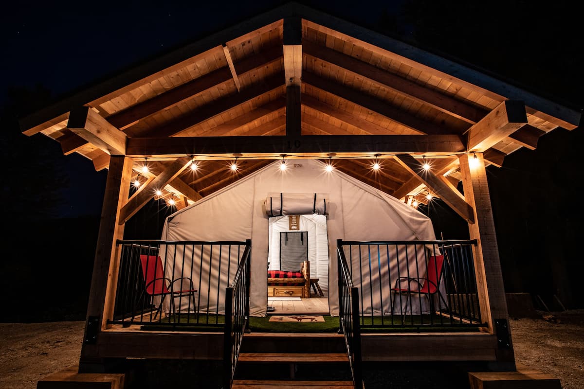A wooden tent structure with a covered entrance and a small seating area inside.