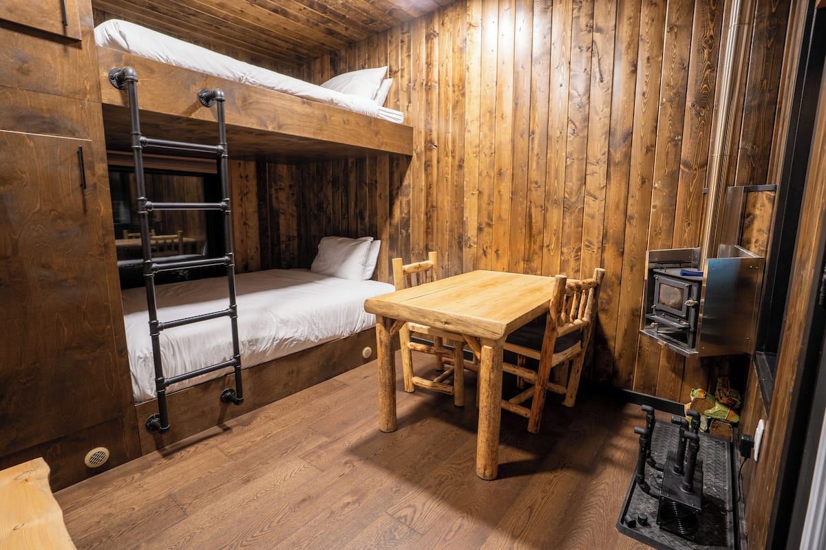 A wooden room with bunk beds, a table, chairs, and a small kitchenette.