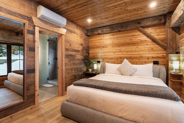 A wooden cabin-style bedroom with a large bed, a walk-in closet, and a bathroom with a shower. - Boulder Mountain Resort (Revelstoke)