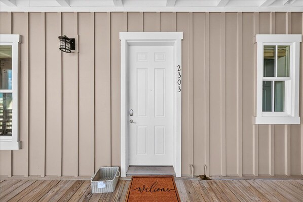 A front door with a number, a welcome mat, and a basket. - Get Gulf & Bay Views@Gorgeous Cinnamon Shore Condo w/ Great Amenities! (Port Aransas)