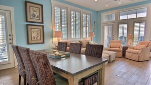 A spacious living room with a large dining table, wicker chairs, a sofa, and two armchairs. - Book 'Coral Sunset,' a Corner Condo w/ 2 Balconies+Cinnamon Shore Amenities (Port Aransas)