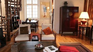 A cozy living room with a wooden staircase, a dining area with a table and chairs, and a large cabinet with a clock. - Charming cozy triplex in trendy Marais (Paris)
