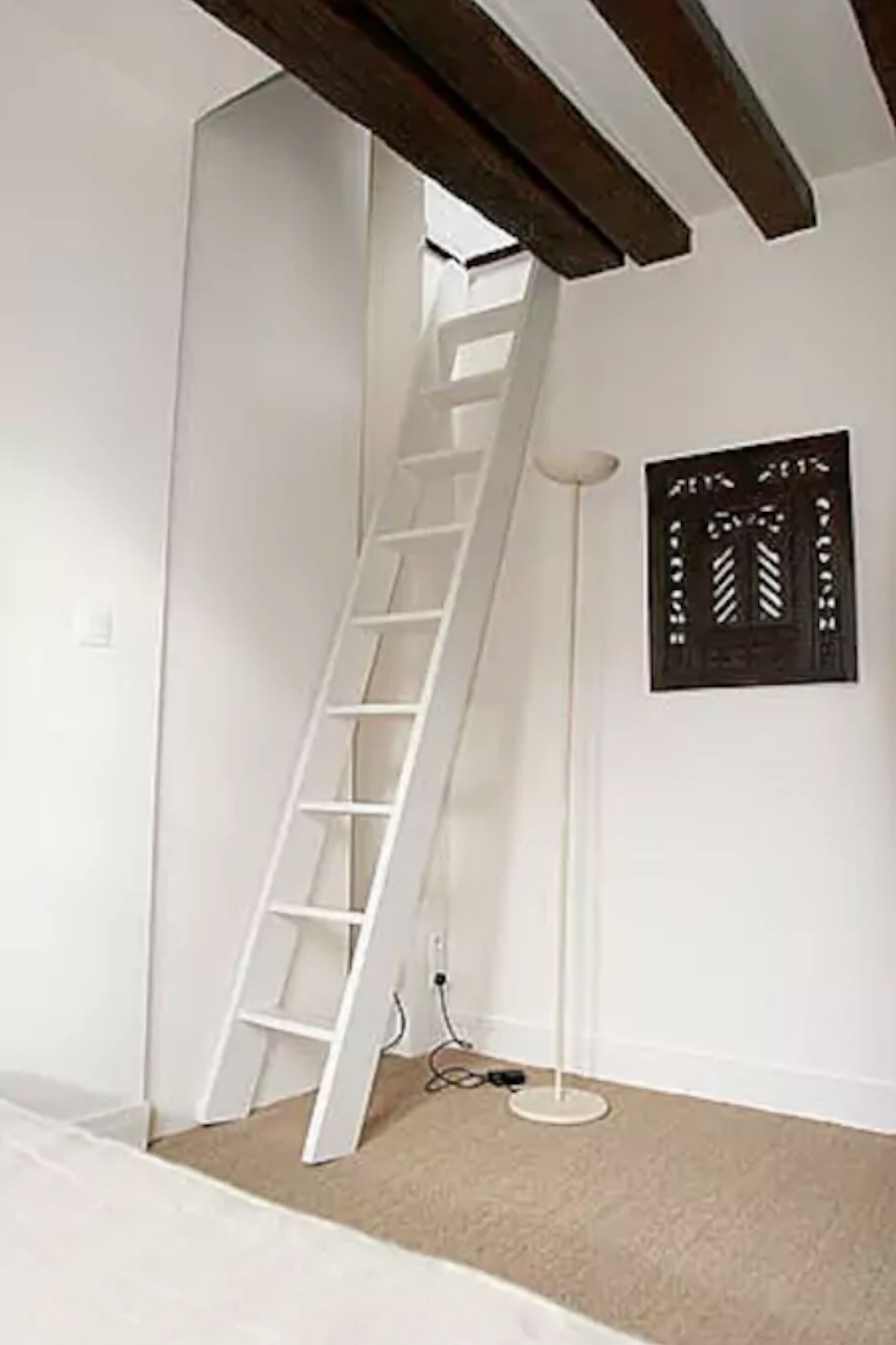 Una habitación con una pared blanca, una lámpara de pie blanca y una escalera blanca apoyada en la pared.