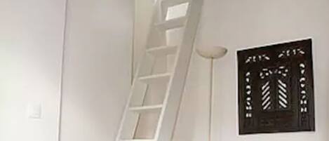 Una habitación con una pared blanca, una lámpara de pie blanca y una escalera blanca apoyada en la pared.