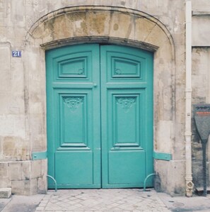 A turquoise double door with decorative panels, set within a stone building with a visible number '21' on the wall.