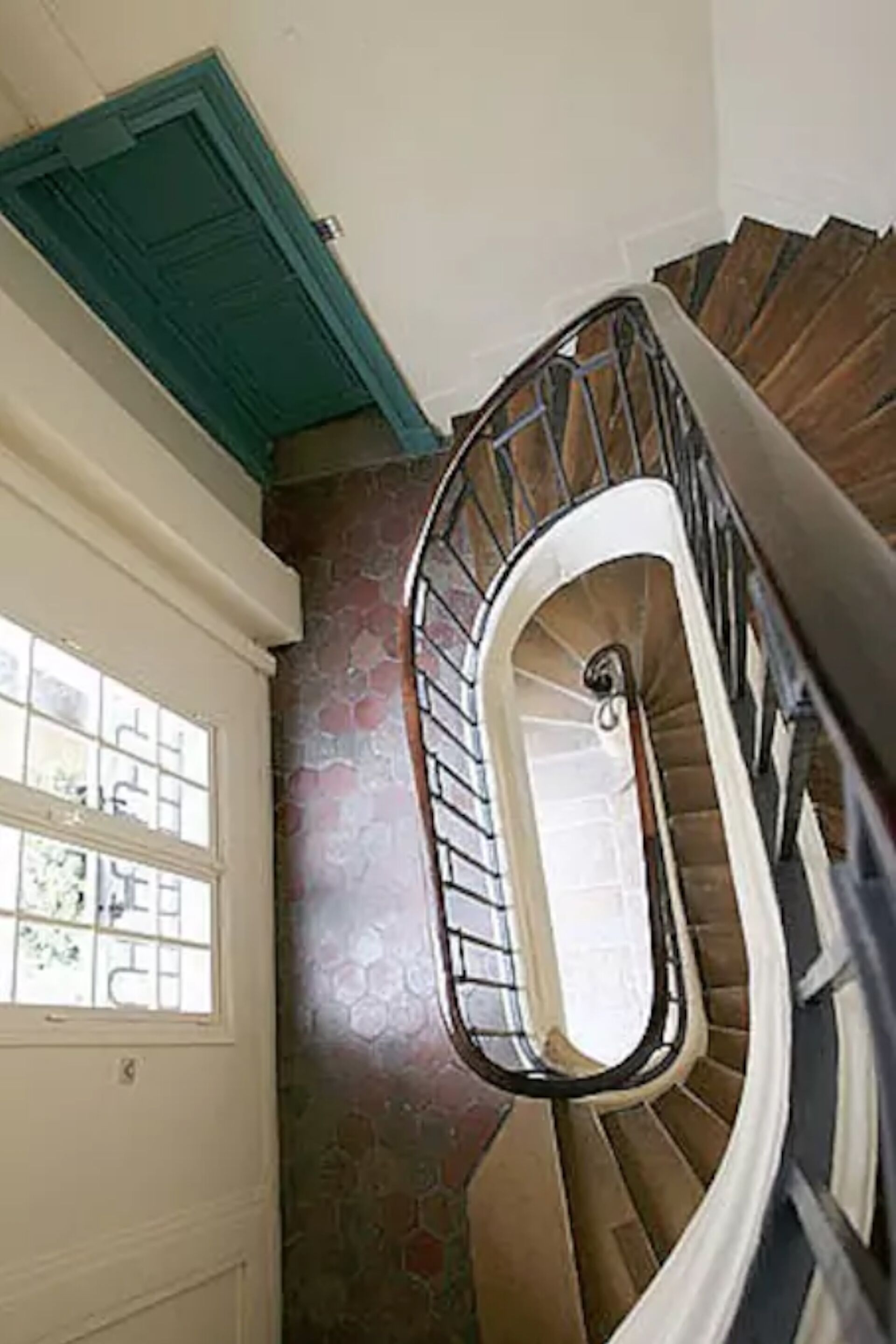Un escalier en colimaçon, avec un mur en pierre et une fenêtre à motifs géométriques.