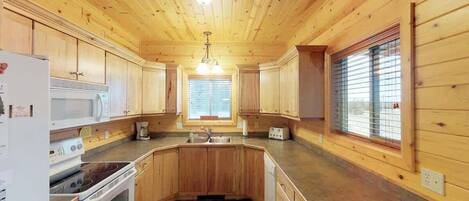 Una cocina con armarios de madera, microondas, estufa y pileta.