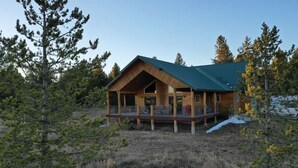 A wooden cabin with a green roof, a deck, and surrounded by trees. - 31 MI to YNP | Fire Pit | Sleeps 10 (Island Park)