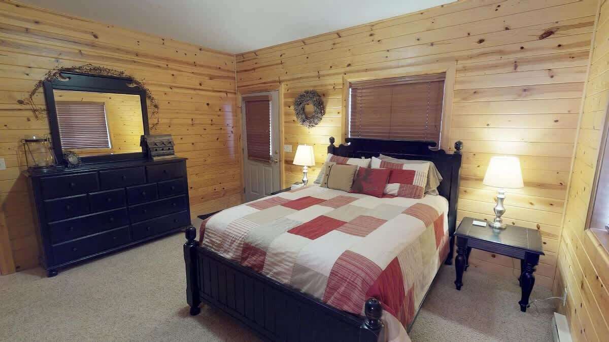Quarto com painéis de madeira, uma cama, penteadeira e duas mesas de cabeceira com abajures.