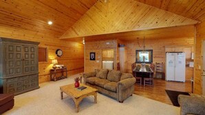 A cozy cabin interior with a wooden ceiling, a sofa, a coffee table, a dining area, and a kitchen. - 31 MI to YNP | Fire Pit | Sleeps 10 (Island Park)