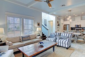 A spacious living room with a sofa, armchairs, and a coffee table. A staircase leads to a kitchen area with modern appliances.