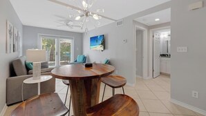 A dining area with a round wooden table and four chairs, a ceiling fan, and a view of the kitchen through an open doorway. - AQUA OASIS at The Truman Annex in Key West (Key West)
