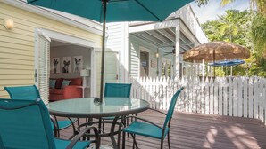 An outdoor patio with a round glass table and teal chairs, a white picket fence, and a thatched umbrella. - AQUA OASIS at The Truman Annex in Key West (Key West)