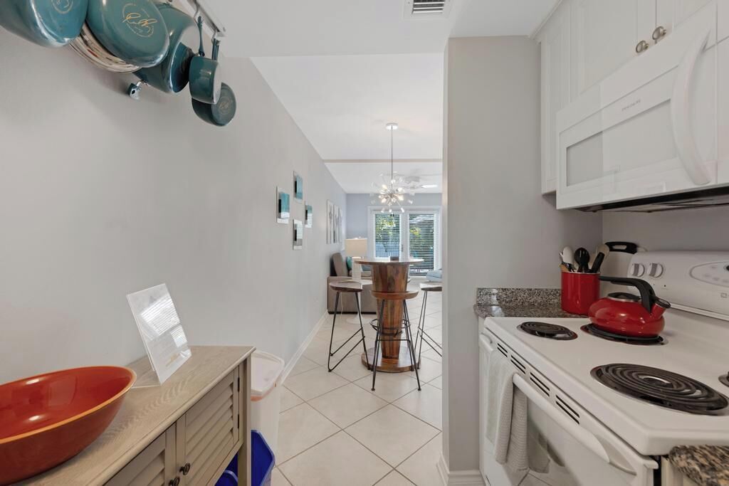 A kitchen with white cabinets, a red kettle, and a wooden dining table with chairs.