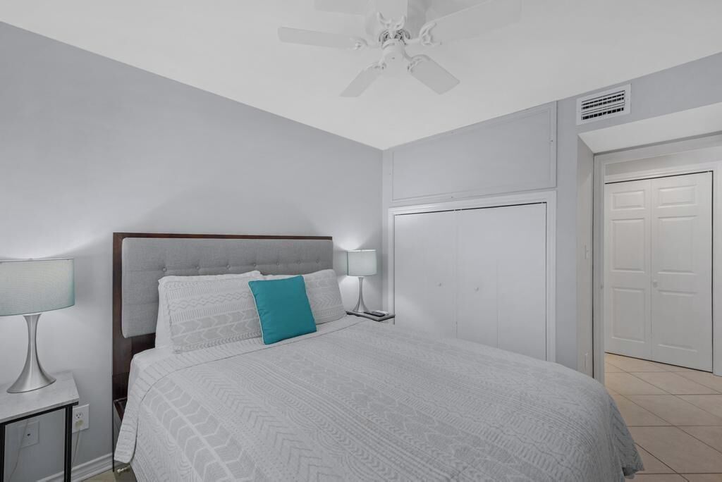 A bedroom with a bed, two bedside tables with lamps, a ceiling fan, and a wardrobe.
