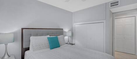 Un dormitorio con cama, dos mesitas de noche con lámparas, un ventilador de techo y un armario.