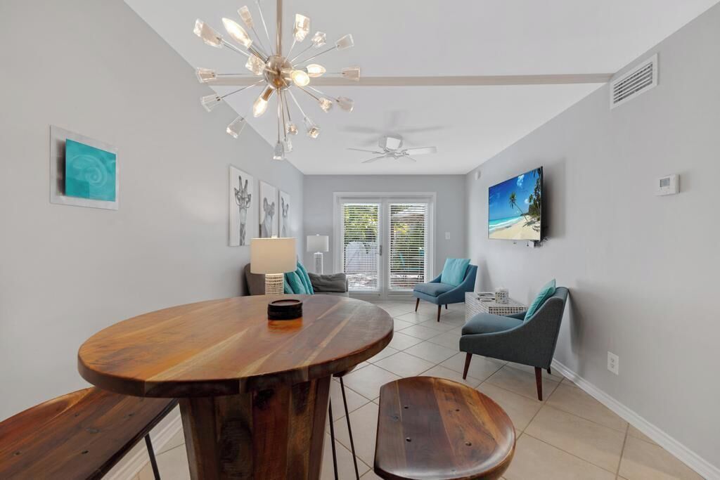 A modern living room with a wooden dining table, two chairs, a ceiling fan, and a TV mounted on the wall.