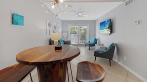 A modern living room with a wooden dining table, two chairs, a ceiling fan, and a TV mounted on the wall. - AQUA OASIS at The Truman Annex in Key West (Key West)