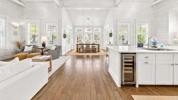A spacious room with a wooden floor, white walls, a dining area with a table and chairs, and a kitchen with white cabinets and a sink. - Breathtaking Home in Cinnamon Shore w/ Access to Resort-Style Amenities (Port Aransas)