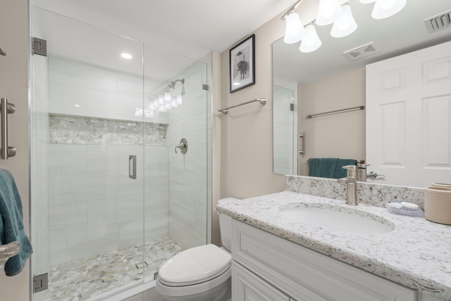 Une salle de bain moderne dotée d’une douche à parois de verre, de toilettes blanches, d’un comptoir en marbre et d’un grand miroir.