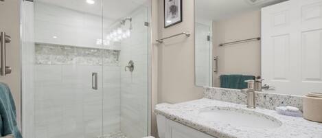 Une salle de bain moderne dotée d’une douche à parois de verre, de toilettes blanches, d’un comptoir en marbre et d’un grand miroir.