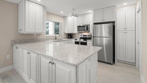 A modern kitchen with white cabinetry, granite countertops, stainless steel appliances, and a window providing natural light.
