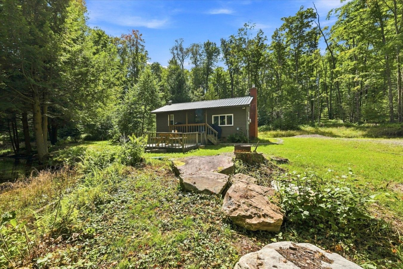 Una cabaña con terraza, rodeada de bosque y zona verde.