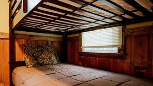 Una cama litera con colchón acolchado, cabecera de madera y ventana con persianas.