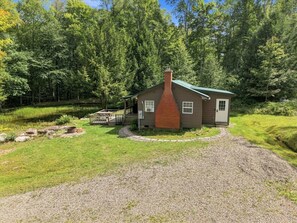 Une petite cabane avec une cheminée en briques, entourée d’une allée de gravier et d’une zone herbeuse.