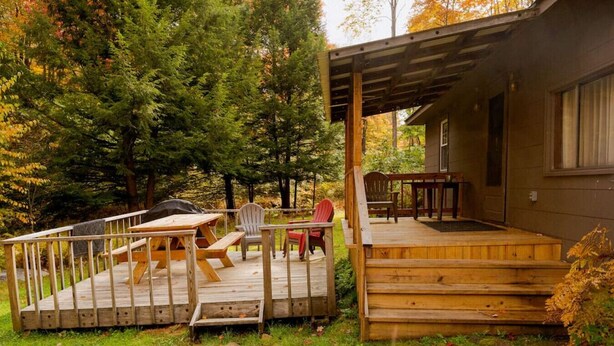 Una terraza de madera con una mesa de picnic y sillas, un espacio de estar cubierto y una casa al fondo.