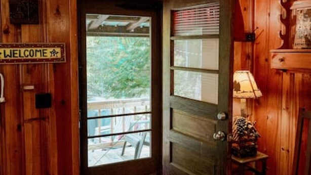 Una puerta de madera con un letrero que dice 'WELCOME', una ventana con persianas, una lámpara y un sillón mecedora.