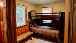 Habitación con literas, ventana, paredes de madera y un banco.