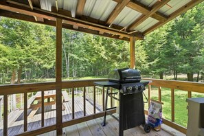 Una terraza techada al aire libre con una parrilla, una mesa y un saco de carbón.
