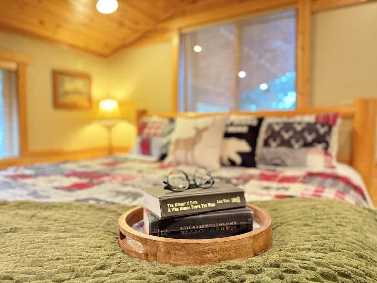 Un dormitori acollidor amb un capçal de fusta, un estriatge acolxat al llit i una tauleta de nit amb llibres i ulleres.