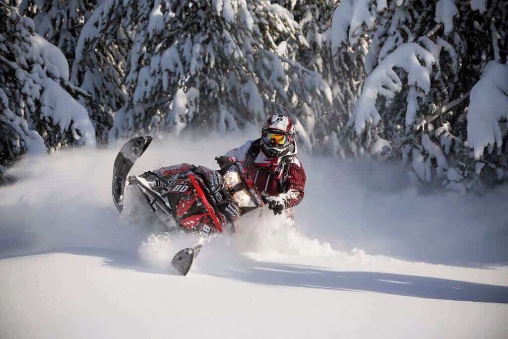 A snowmobile in motion on a snowy path with trees in the background.