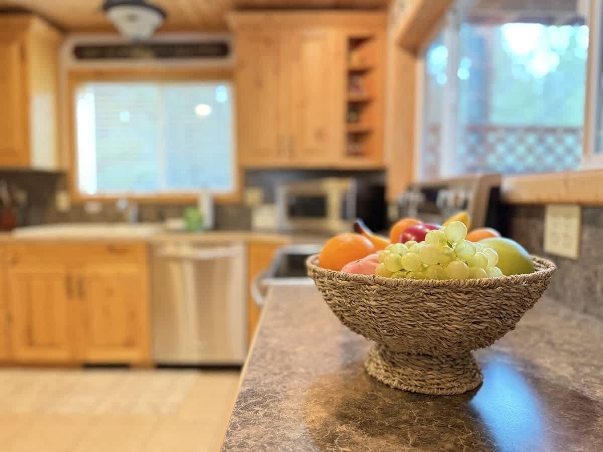 A kitchen with wooden cabinets, a granite countertop, and a wicker bowl filled with fruits.