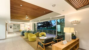 A modern lobby with a wooden ceiling, seating area with yellow chairs, a reception desk, and a view of the outdoors. - Direct Oceanfront Waikiki!  Parking at Waikiki Shore included! (Honolulu)