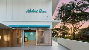 A hotel entrance with a sign reading "Walkiki Shore," a wooden fence, and a view of palm trees and a sunset. - Direct Oceanfront Waikiki!  Parking at Waikiki Shore included! (Honolulu)