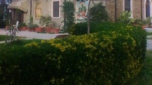 Ein gepflegter Heckenstreifen vor einem Gebäude mit einer Stein-Fassade und einem Fenster mit Rollo.