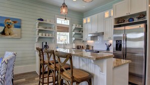 A kitchen with wooden bar stools, a stainless steel refrigerator, and a large island with a sink.