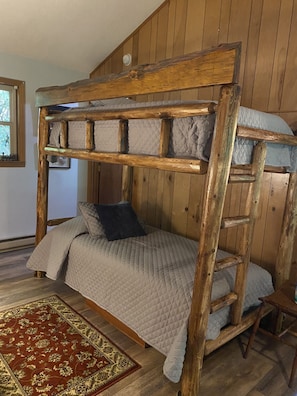 Una cama litera con escalera de madera, colchón acolchado y alfombra estampada.