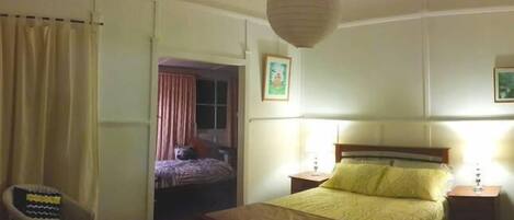 A bedroom with a bed, a chair, a nightstand, and a hanging light fixture.