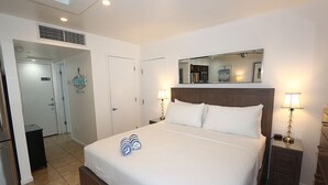 A hotel room with a large bed, bedside lamps, a mirror above the bed, and a door leading to a bathroom. - Oceanfront Oasis – Longboat Key 226 by RVA (Longboat Key)