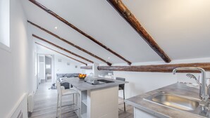 Une cuisine moderne dotée d’un îlot central, de meubles blancs et de poutres apparentes en bois.