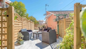Un espace extérieur aménagé en terrasse, avec des meubles en osier, des plantes en pot et une clôture en bois.