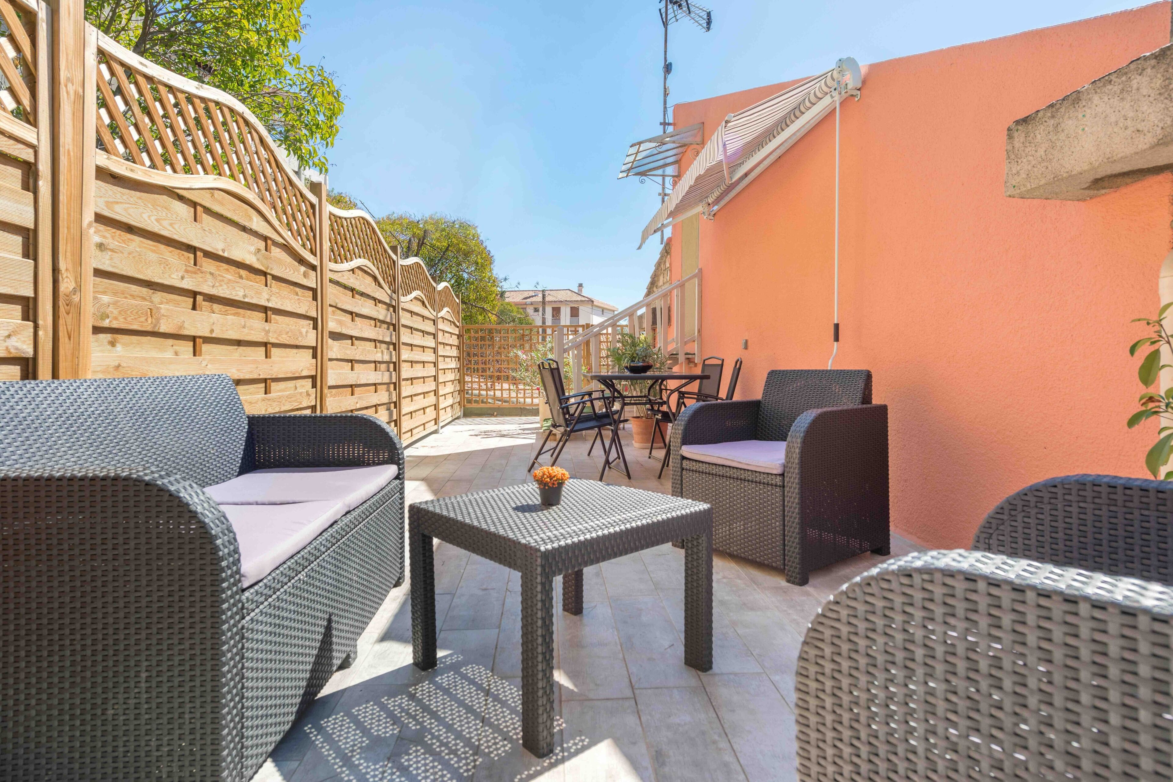 Patio esterno con mobili in vimini, un tavolo e un recinto in legno.